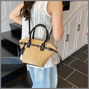 Detail of woven straw tote bag with black leather handles and trim shown on model