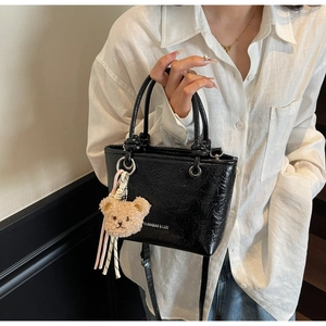 Detail of black glossy bucket bag with fuzzy bear charm and stripe ribbon accessory