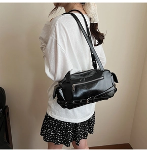 Detailed back view of a black glossy leather shoulder bag with silver multi-zippers on a model