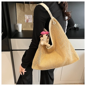 Detail of beige woven tote bag with cream leather trim and a small plush dog charm