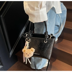 Detail of black textured bucket bag with teddy bear charm and brand logo on side
