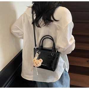 Detail of glossy black patent leather bucket bag with a cute plush bear charm