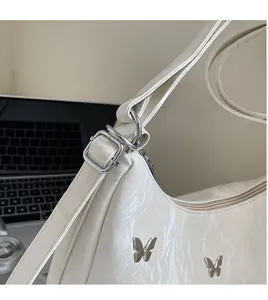 Detail of silver butterfly ornament and smooth adjustable strap on a white shoulder bag