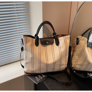 Detail view of large striped canvas tote bag featuring black leather flap and shoulder strap