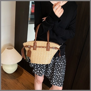 Close-up of handwoven straw tote with brown leather strap and metal buckle detail