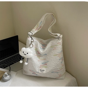 Detail of white quilted tote bag with colorful embroidery and plush cloud charm