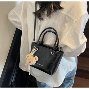 Detail of black glossy bucket bag with brand logo and cute plush bear charm decoration