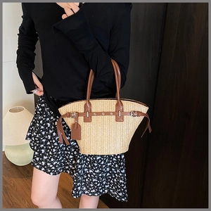 Detail view of woven straw tote bag with brown leather handles and metallic buckle accents