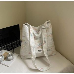Detail of cream quilted tote bag with colorful embroidery on a minimalist white desk