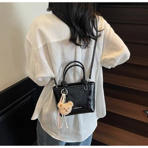 Detail of black glossy wrinkled leather tote bag with plush bear charm and long strap