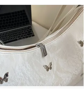 Detail of a white crescent shoulder bag featuring smooth metal zipper and butterfly buckle