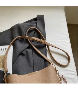 Detail of beige lychee leather bag featuring gold hardware and a decorative silk scarf