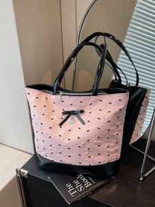 Grande borsa tote rosa e nera con fiocco e ciondolo a cuore posata su un tavolo