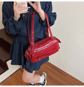 Detail view of a glossy red leather pillow bag with silver eyelets and buckle strap