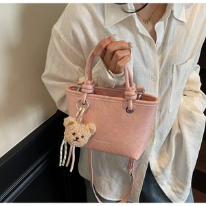Detail of pink pleated bucket bag with plush bear charm and DUMABAO logo on model