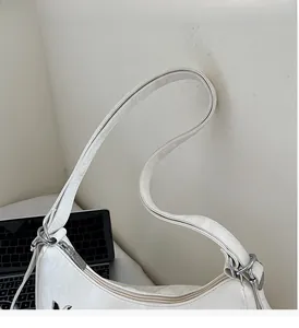 Detail of white half-moon shoulder bag showing zipper closure and durable top handle