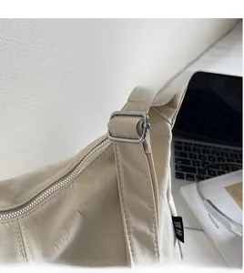 Detail view of the beige canvas bag's adjustable shoulder strap with metal buckle and zipper
