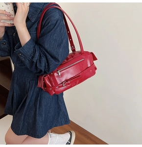 Detail of red glossy pillow bag with silver zippers and buckle straps worn on shoulder
