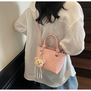 Pink textured leather bucket bag with bear pendant shown on a crossbody model