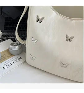 Close-up of cream shoulder bag featuring decorative silver butterfly metal buckles