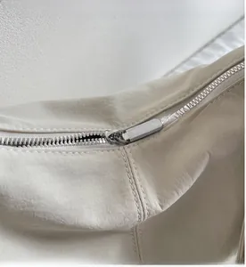 Detail of a smooth silver zipper closure on a cream-colored nylon crescent bag