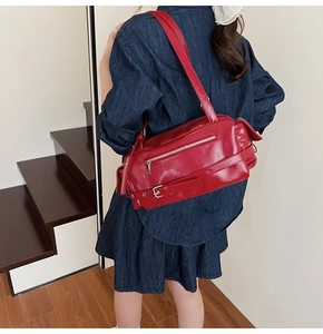 Detail of red leather shoulder bag with decorative zippers and buckles worn by a model