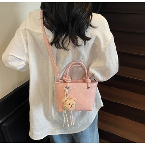 Pink lychee texture mini tote bag with plush bear charm worn as a crossbody bag