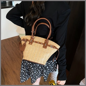 Straw tote bag featuring brown leather straps and metal buckle on a model's shoulder