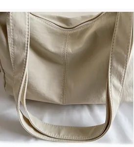 Detailed close-up of light beige nylon tote bag material with stitching and silver zipper