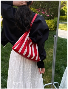 Détail du sac cabas en tricot rayé rouge et blanc porté à l'épaule dans un jardin