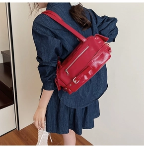 Close-up of a red glossy leather pillow bag featuring silver zippers and industrial buckle