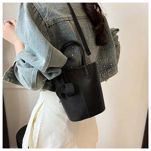 Detail of black pebbled leather bucket bag styled as a crossbody on a denim jacket