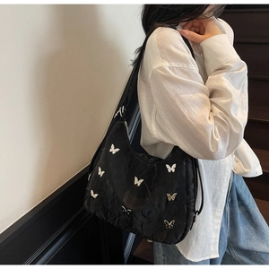 Chic black shoulder bag with silver butterfly patterns worn by a model in casual style