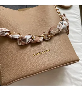 Detail of lychee pattern leather handbag with scarf-wrapped chain handle and gold logo