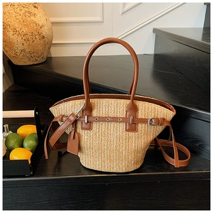 Close-up of beige woven straw tote bag with brown leather handles and decorative straps