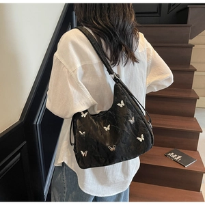 Modern black hobo bag with silver butterfly charms on a model climbing stairs