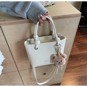 Close-up of a mini white bucket bag with textured pleats and a cute brown bear charm