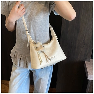 Détail d'un sac à bandoulière crème avec texture froissée, logo argenté et breloque ours