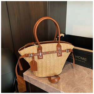 Detail of woven straw tote bag featuring brown leather straps and metallic buckle accents