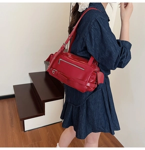 Model wearing a red patent leather pillow bag with adjustable strap on a denim dress