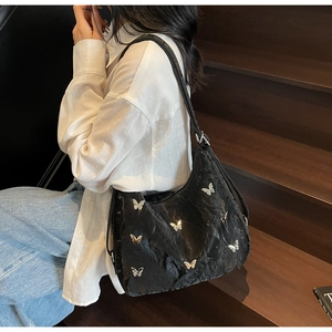 Detail of black pleated hobo bag featuring silver butterfly metal charms and matte texture