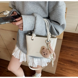 Detail of cream pleated patent leather bucket bag with plush bear charm and handle