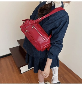 Detail of bright red biker crossbody bag with silver buckles and metallic eyelets