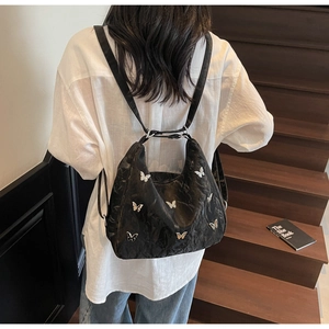 Detailed view of black hobo backpack with silver butterfly patches on a female model