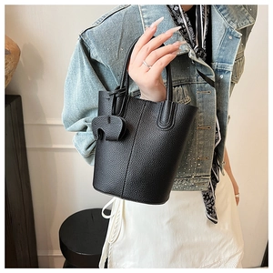 Detail of black pebbled leather bucket bag with cute elephant charm held by hand