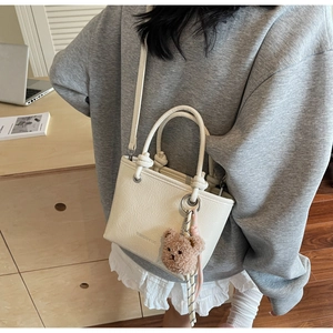 Detail of cream white bucket bag with pleated texture and cute brown plush bear charm