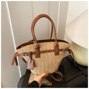Detail of hand-woven straw tote bag with brown leather handles and adjustable shoulder strap
