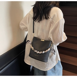 Détail du sac seau en cuir noir avec poignée en foulard de soie et logo doré chic