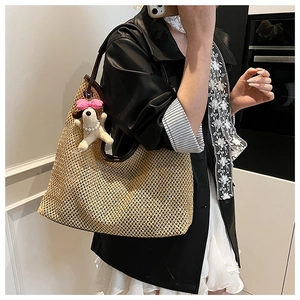 Close-up of woven straw tote bag featuring leather trim and cute puppy plush pendant