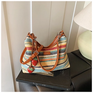 Détail du sac bandoulière tissé coloré avec logo en cuir et breloques fraises